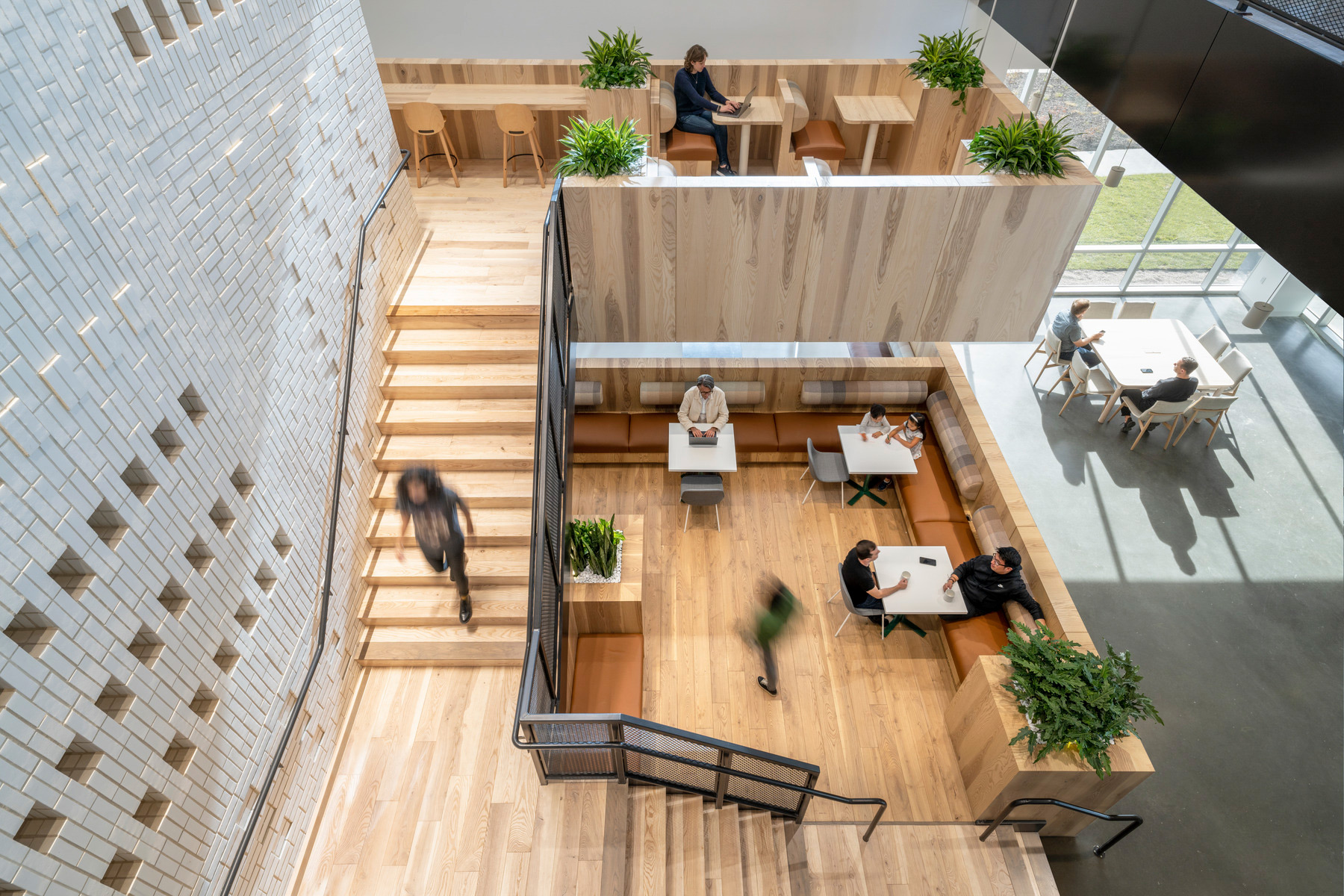 A view looking down on an interior staircase with cafe-style seating and booths with people working on laptops and chatting.