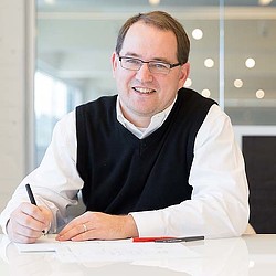 A man wearing glasses and a white shirt sitting at a table.