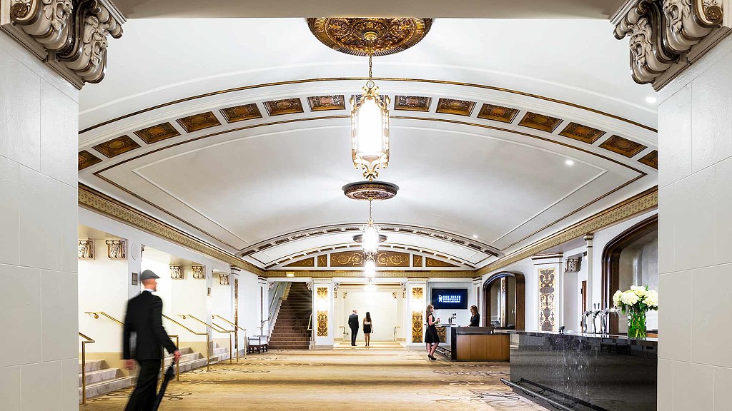 A large white room with a chandelier and people walking around.