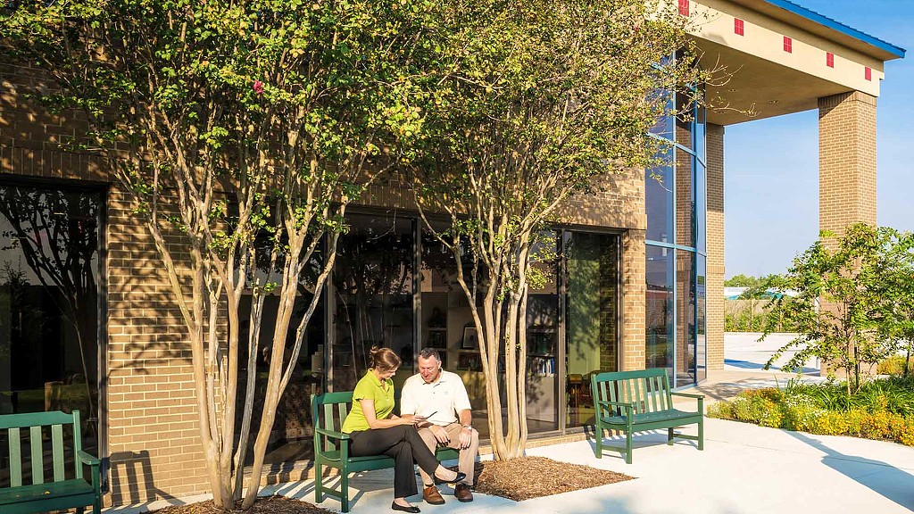 A man and woman sitting on green chairs outside a building.