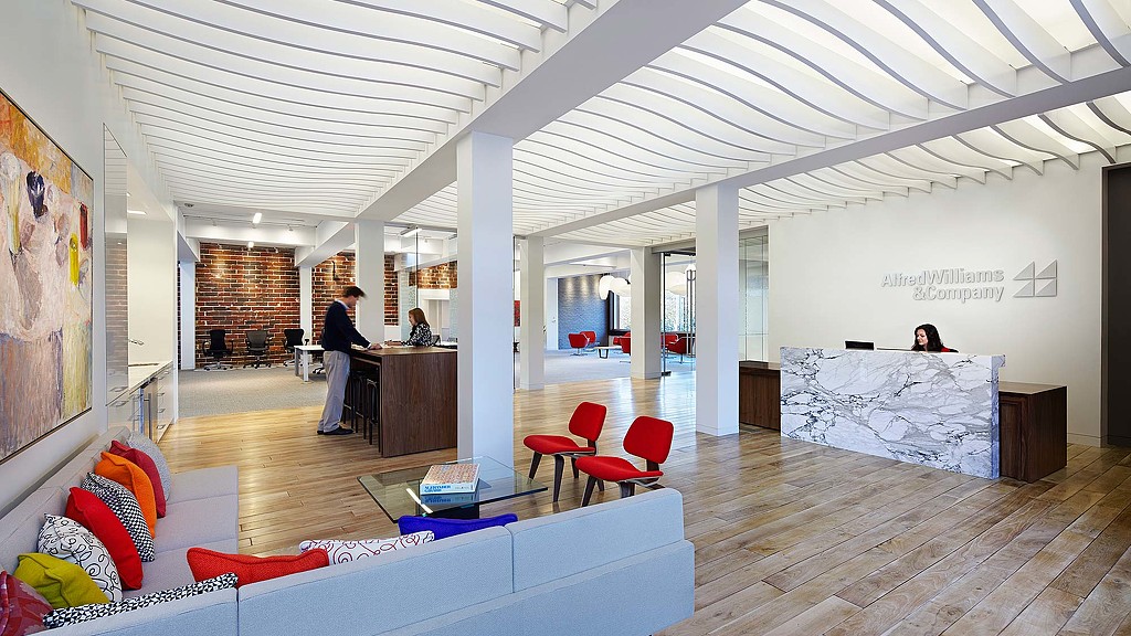 A room with a wood floor and a wood floor with a desk and chairs and a person standing.