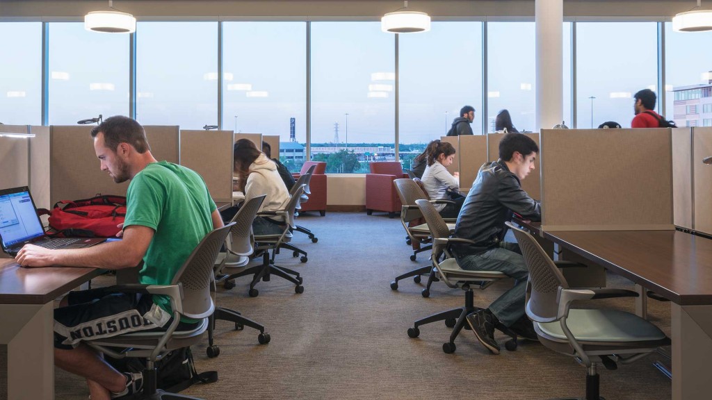 A group of people sitting at desks in a room with large windows.