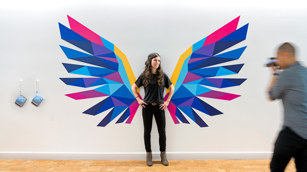 A person standing in front of a wall with a colorful design.